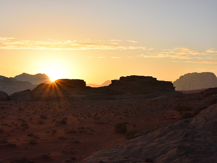 Sun rising up from behind red rock mountains in Wadi Rum desert, Jordan